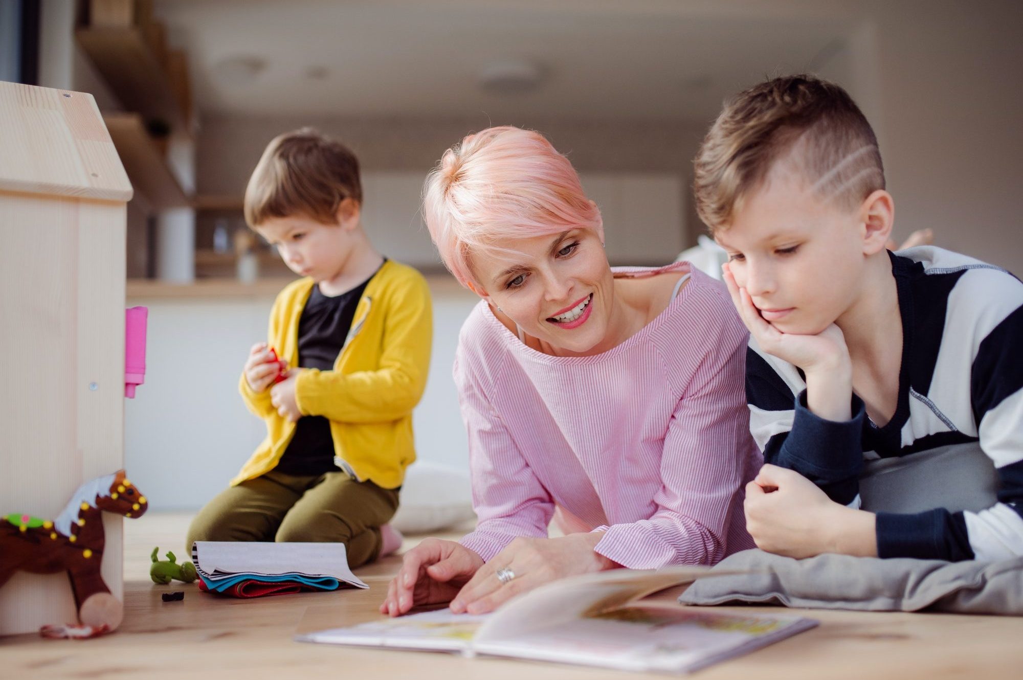 a-young-woman-with-two-children-reading-book-and-playing-on-the-floor--e1619662218134.jpg